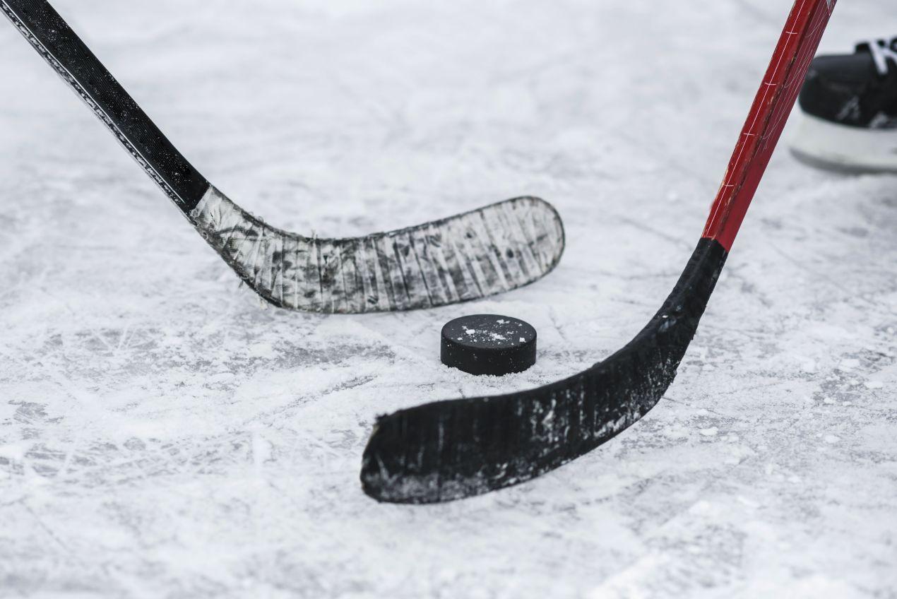 Eishockey Puck liegt zwischen zwei Eishockeyschlägern bei Spielbeginn auf der Eisfläche