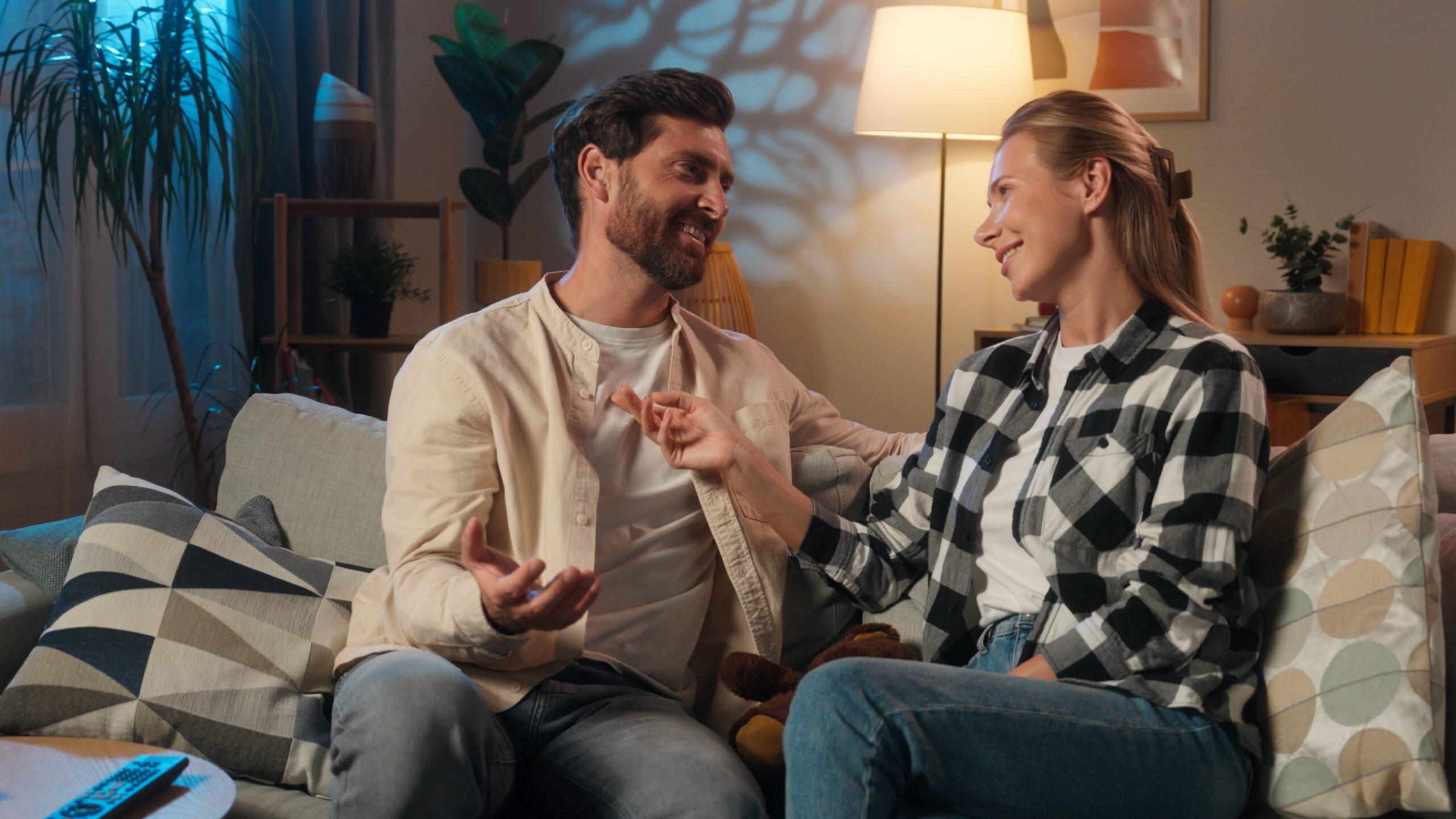 Paar sitzt gemeinsam auf dem Sofa und spricht ueber Beziehungsthemen wie gemeinsame Entscheidungen und Partnerringe