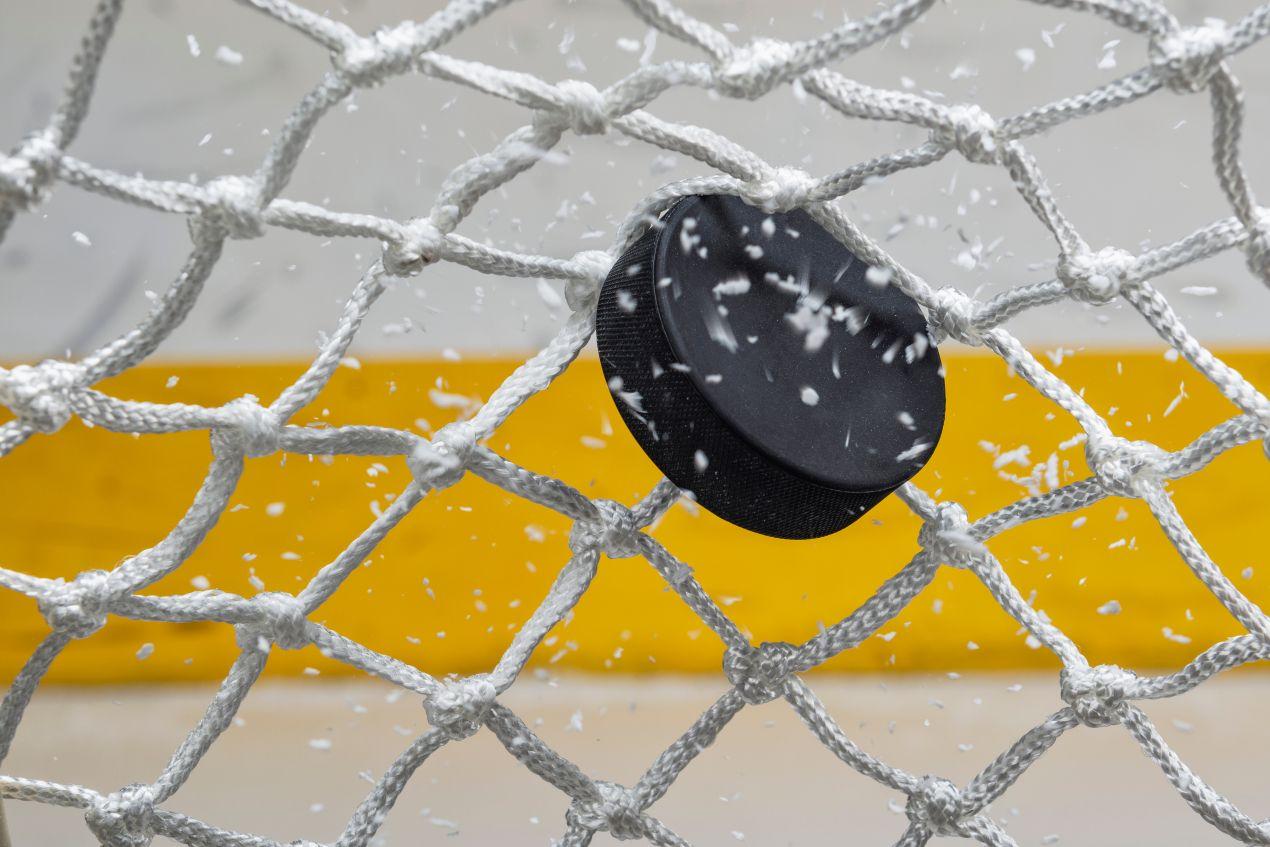 Eishockey Puck durchschlägt Netz mit Eissplittern nach Torschuss auf dem Eis