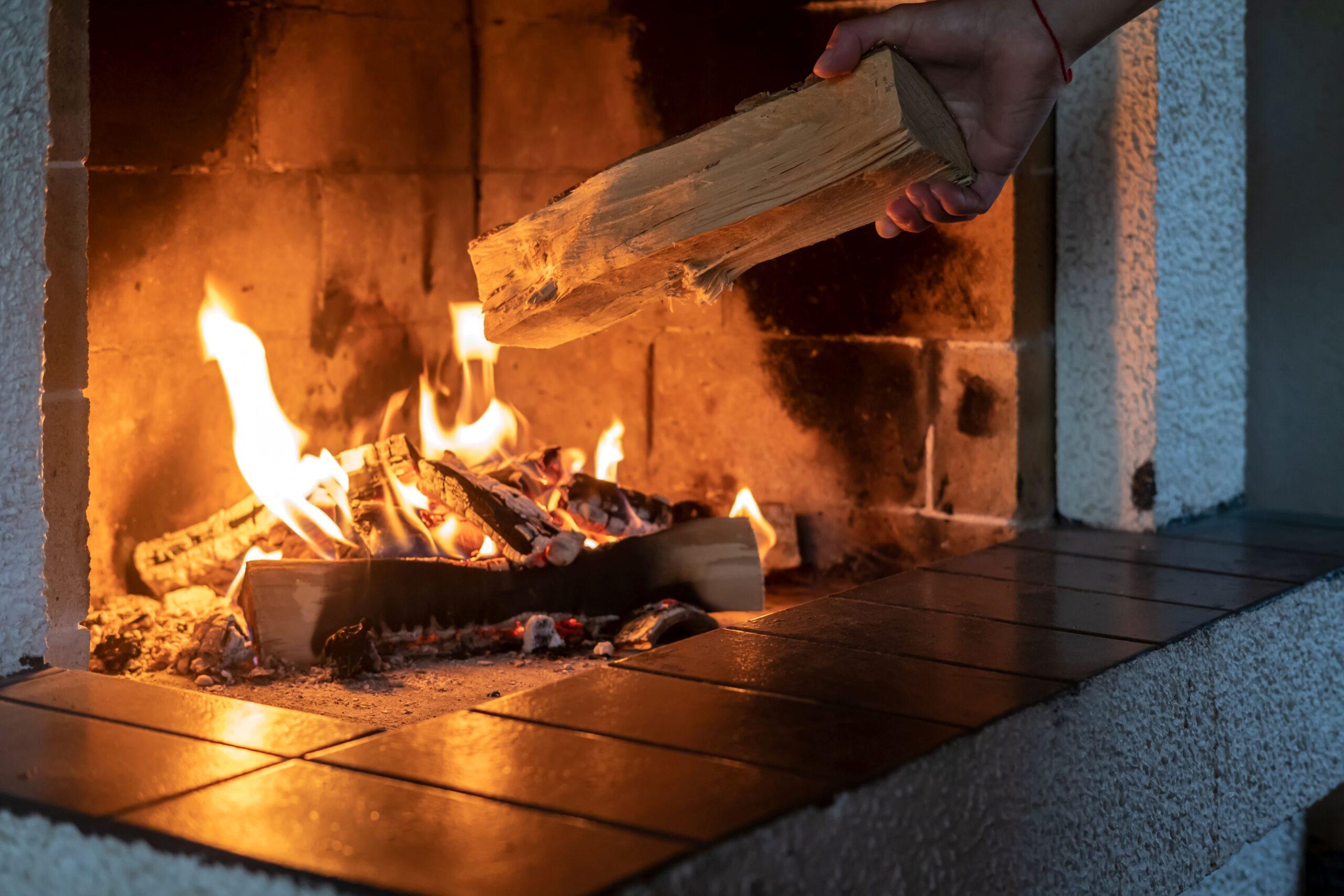 Person legt ein Scheit in den brennenden Kamin