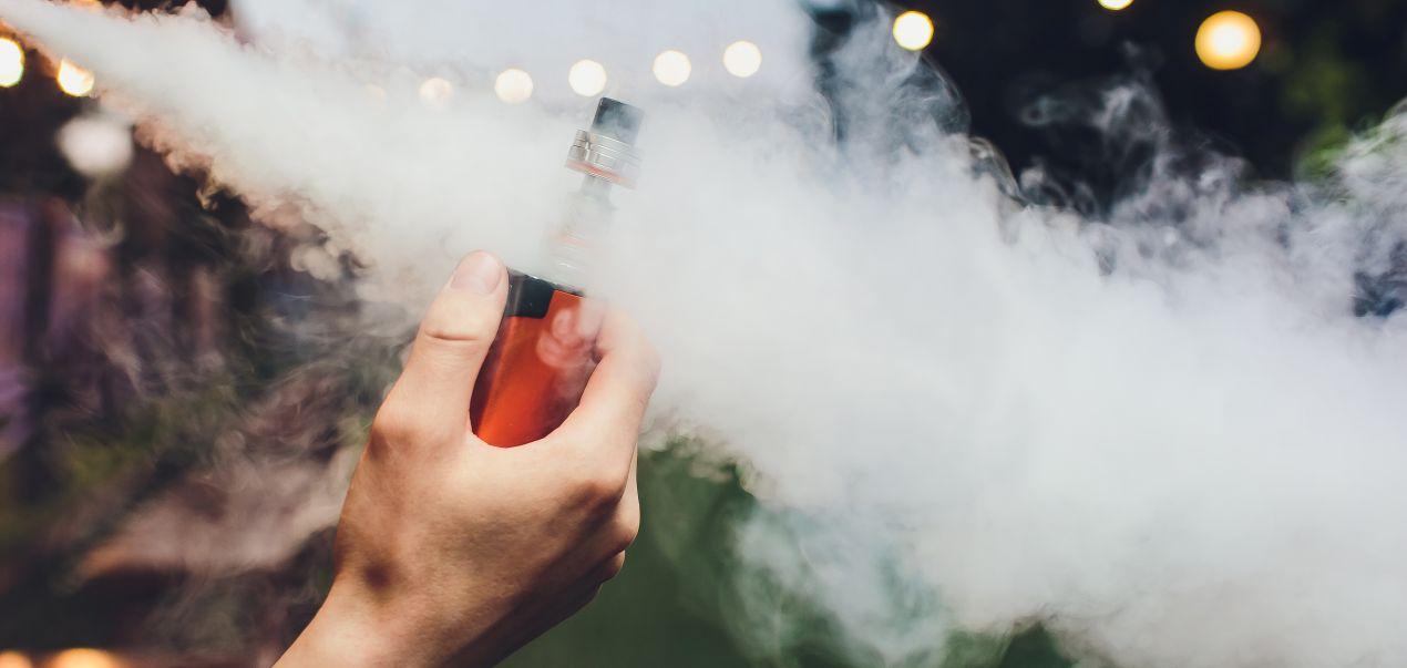 Hand haelt E-Zigarette mit Elfliq Liquid und produziert dichte Dampfwolke im Freien