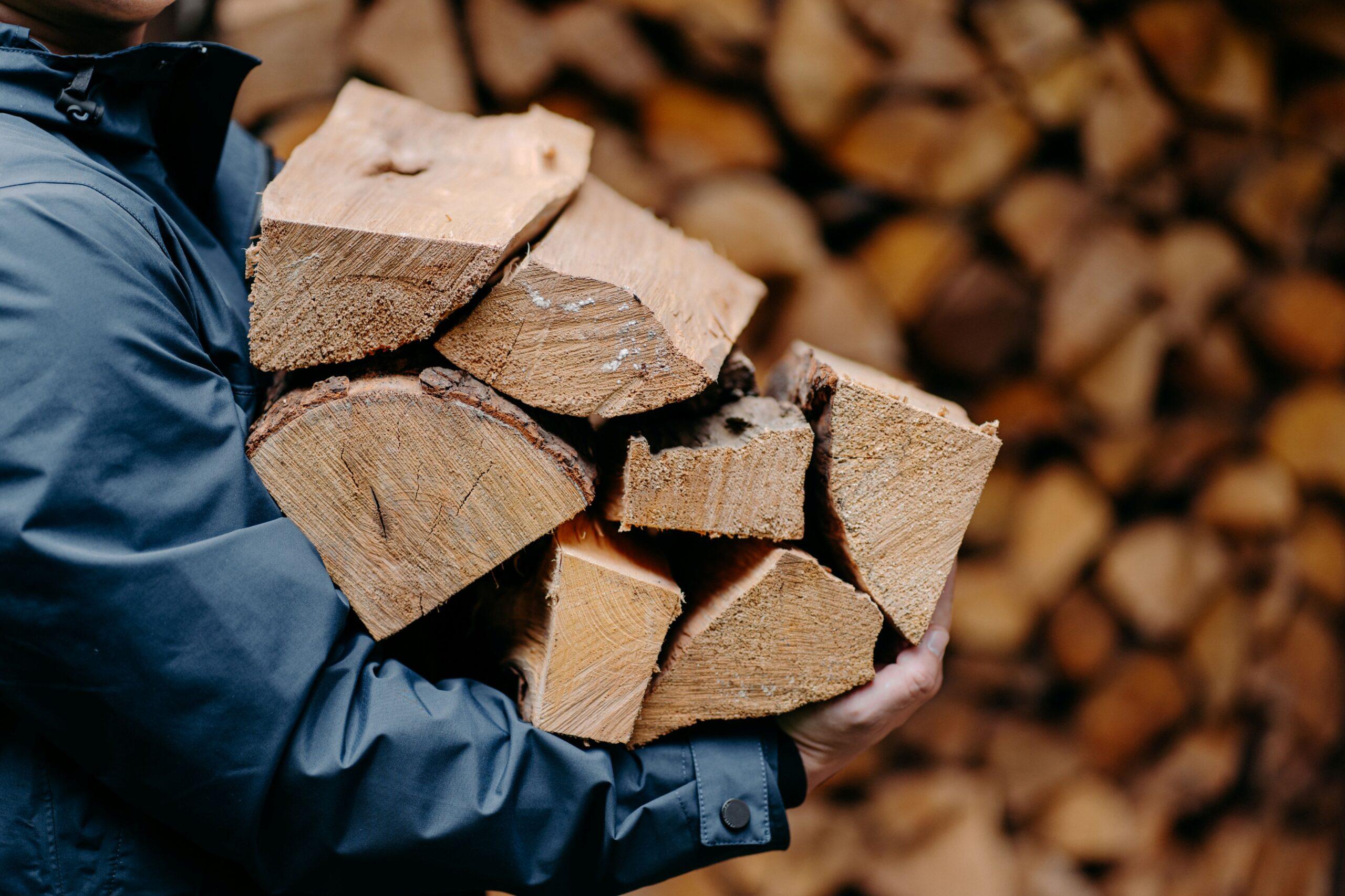 Brennholz bestellen Freising: Person trägt frisches, gespaltenes Holz vor Lagerstapel